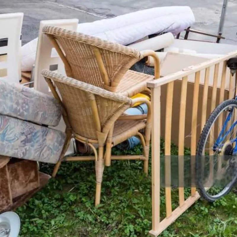 Ein Haufen Möbel und Haushaltsgegenstände, darunter Korbstühle, eine alte Matratze, weiße Plastikstühle und ein Bettgestell aus Holz, liegt draußen auf dem Rasen.